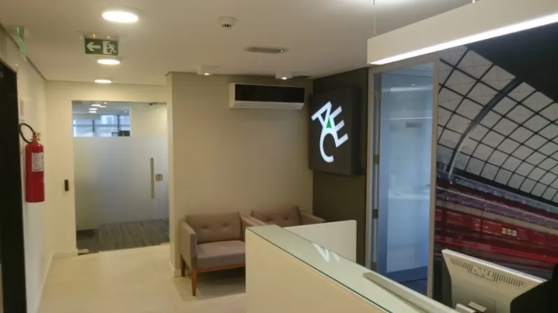 Recepção do escritório ACE em Belo Horizonte, com logotipo iluminado, balcão branco, sofás e porta de vidro jateado