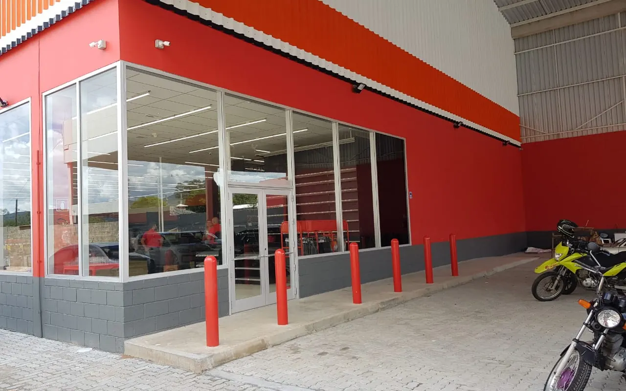 Fachada envidraçada da loja Autozone em Atibaia, com paredes vermelhas, frades de proteção e calçada de piso intertravado