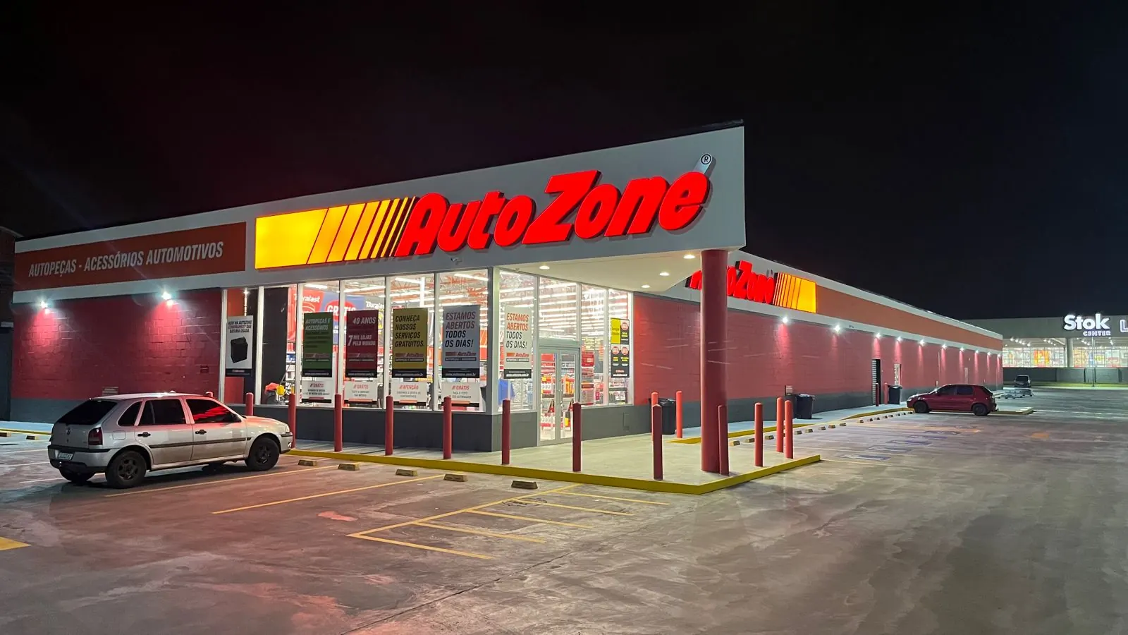 Fachada da loja Autozone em Canoas à noite, com letreiro iluminado, vitrine envidraçada e estacionamento em primeiro plano