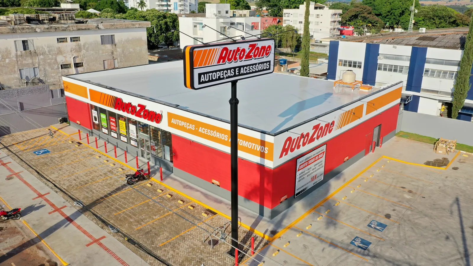 Vista aérea da loja Autozone em Passos, pronta, com totem Autopeças e Acessórios, fachada vermelha, branca e laranja e estacionamento sinalizado
