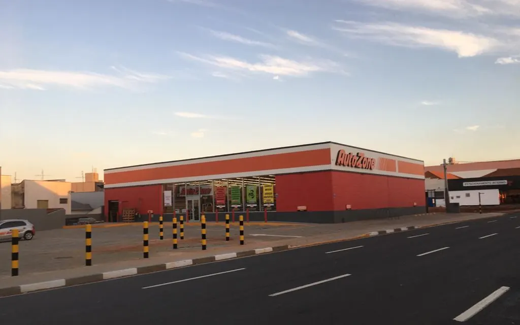 Loja Autozone em Piracicaba ao entardecer, fachada vermelha e laranja com letreiro, vista da avenida