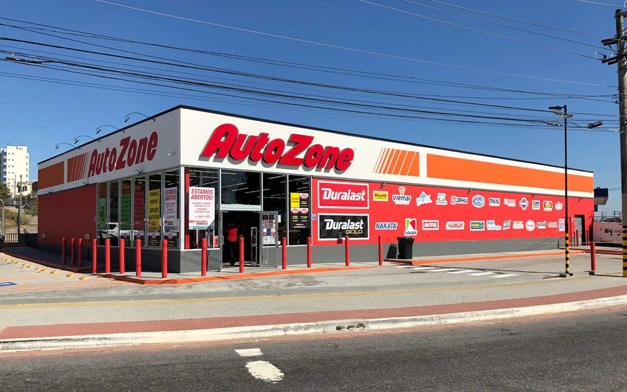 Fachada da loja Autozone em São José dos Campos, com letreiro vermelho e laranja, vitrines e calçada vista da rua sob céu azul