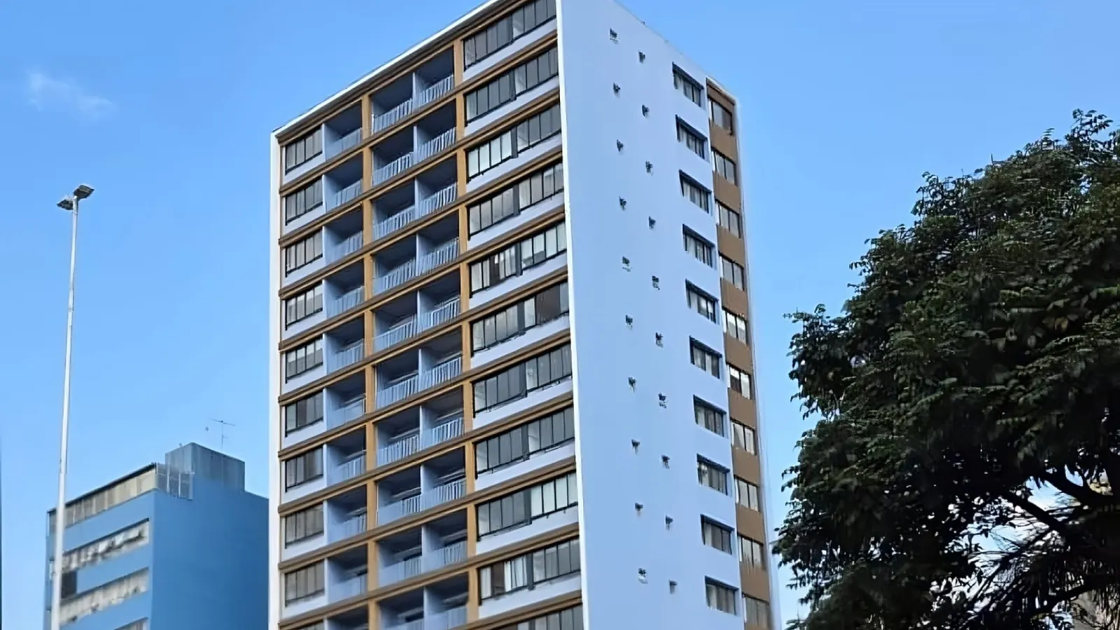 Fachada revitalizada do Edifício Artin Kalaigian, prédio residencial de 14 andares pintado em azul claro e ocre, com varandas, sob céu azul