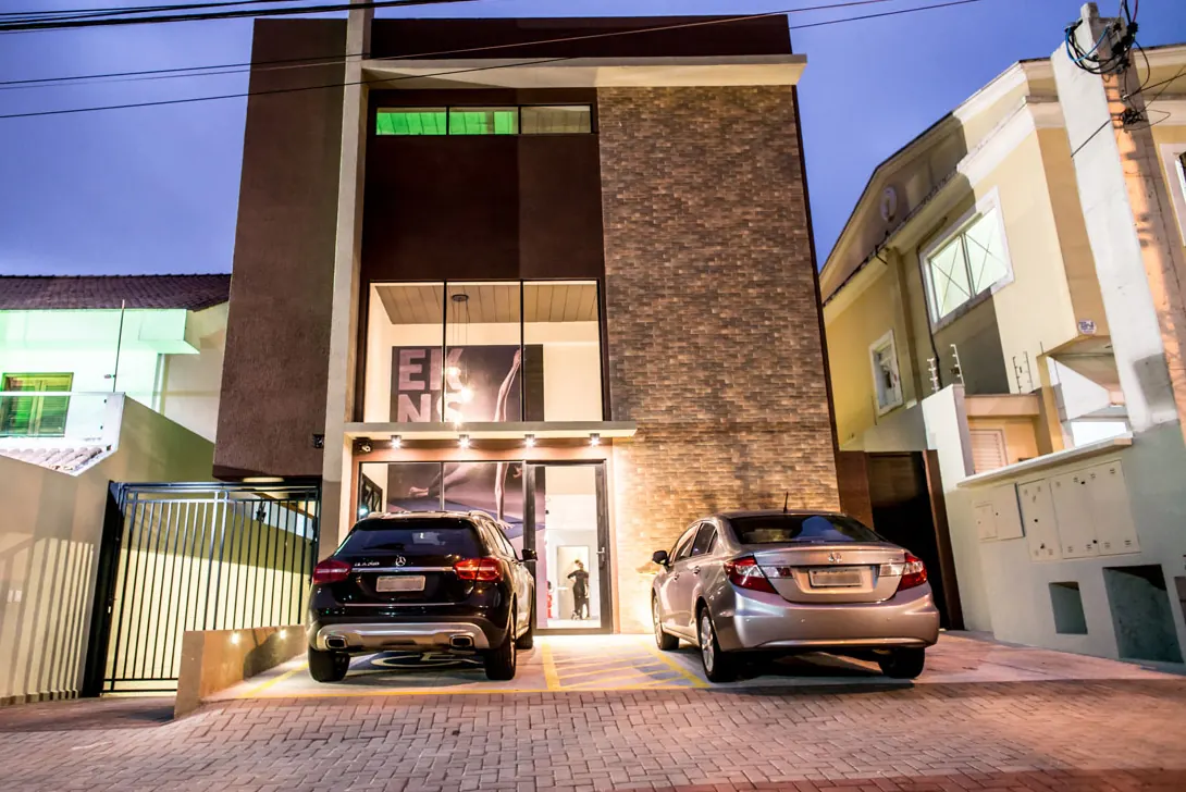 Fachada da unidade Ekness em São José dos Campos ao entardecer, com revestimento em tijolo aparente, vidro em pé-direito duplo e iluminação de destaque