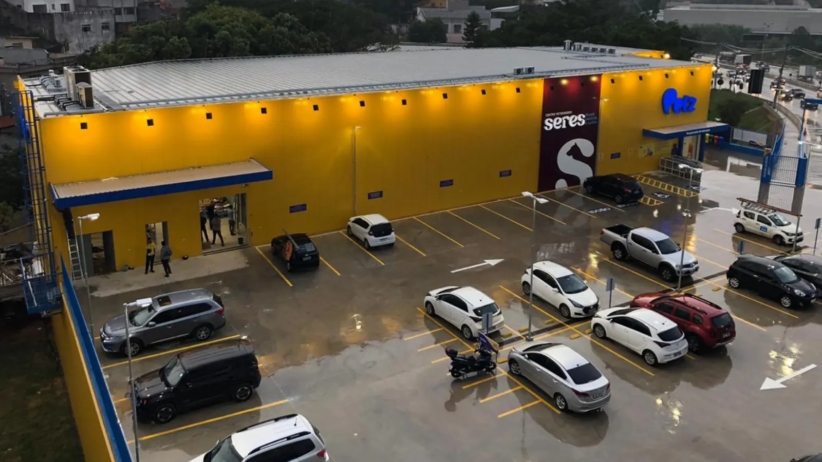 Vista aérea da loja Petz Cotia com fachada amarela iluminada, Centro Veterinário Seres e estacionamento