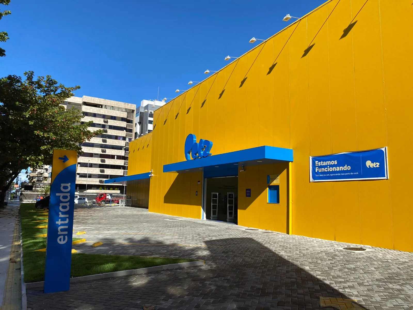 Entrada da loja Petz em Maceió com fachada amarela, marquise azul, totem de entrada e céu azul